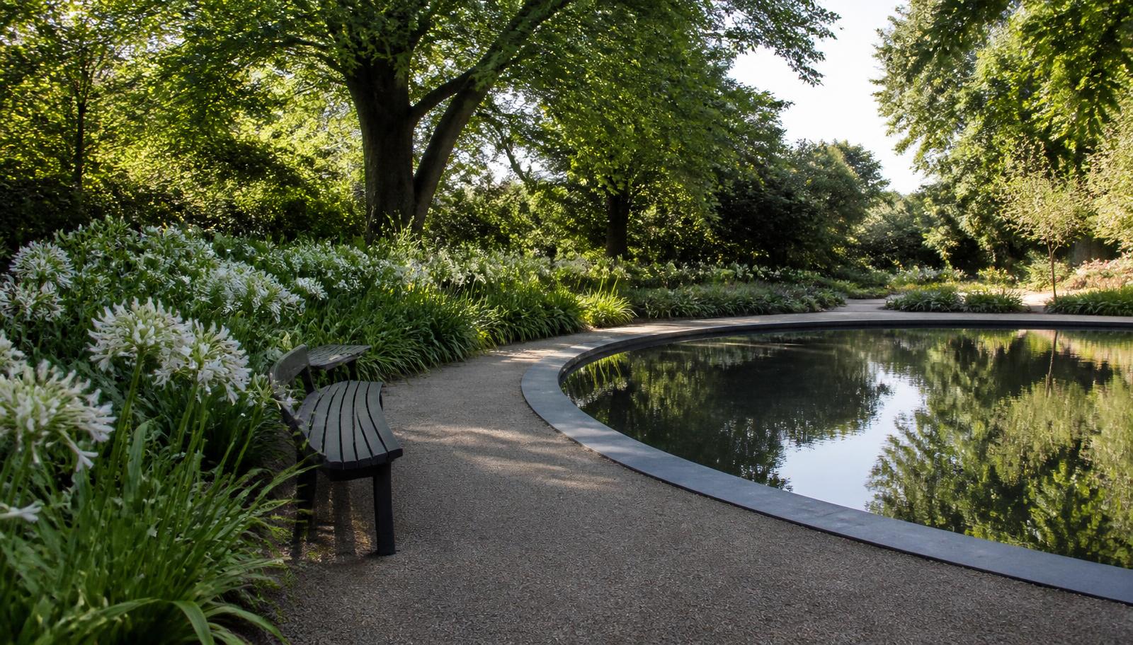 Curved pathway beside a reflecting pond with white agapanthus in a memorial garden